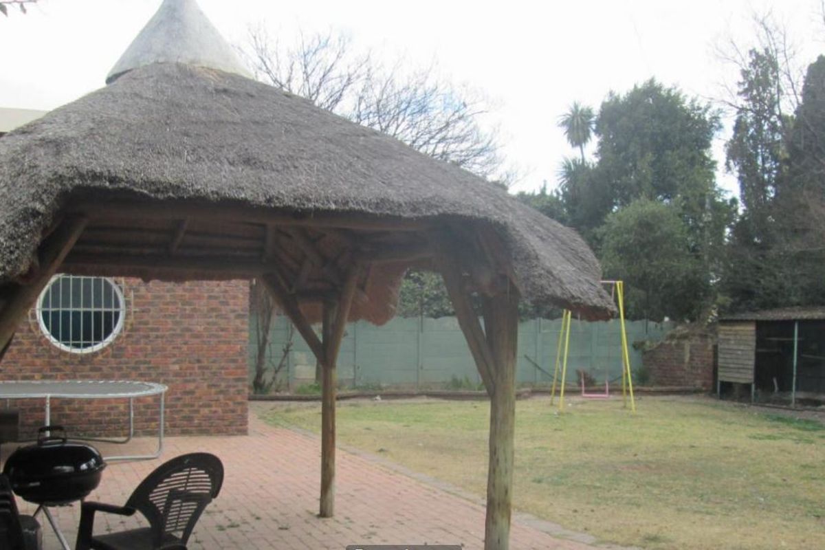A rear garden area featuring a thatched lapa structure, brick paving, and a brick boundary wall in a residential backyard setting.