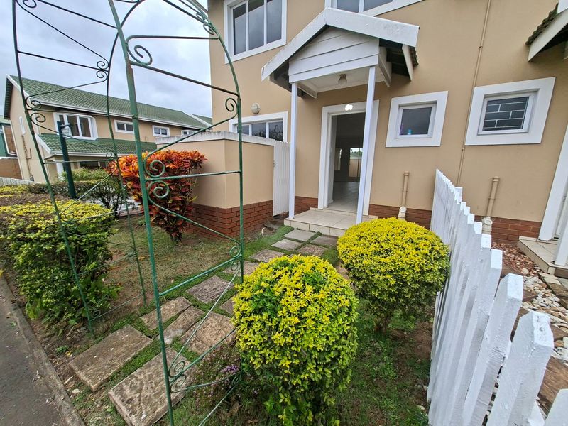 Front entrance of a townhouse featuring a covered porch, paved walkway, and a small garden area with a white picket fence.