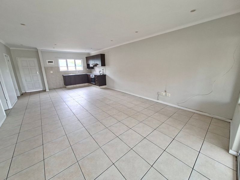 Spacious open-plan living and kitchen area featuring tiled flooring, recessed lighting, and dark-toned built-in cabinetry with integrated oven and extractor fan.