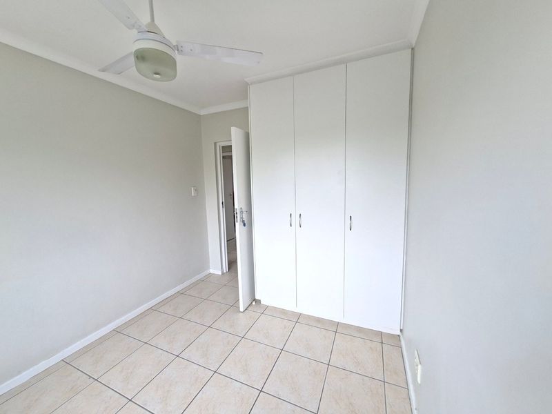 A clean, empty bedroom featuring neutral tiled flooring, built-in cupboards, and a ceiling fan, offering a blank canvas for personalization.