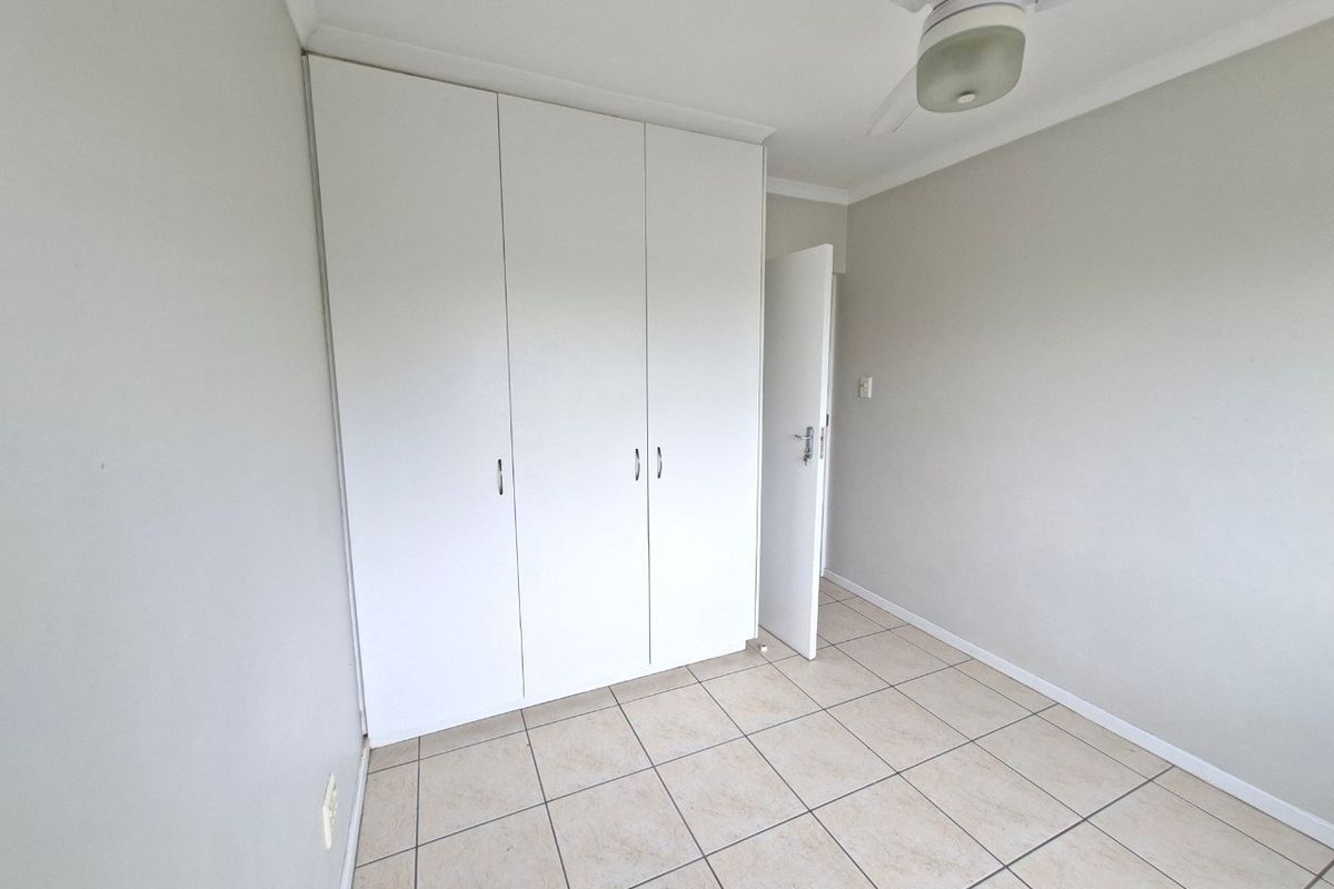 A clean, empty bedroom featuring neutral tiled flooring, built-in white cupboards, and a ceiling fan, providing a blank canvas for personalization.