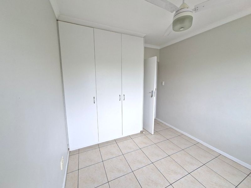 A clean, empty bedroom featuring neutral tiled flooring, built-in white cupboards, and a ceiling fan, providing a blank canvas for personalization.