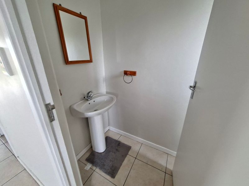 A compact guest bathroom featuring a white pedestal basin with a chrome mixer tap and neutral floor tiling.