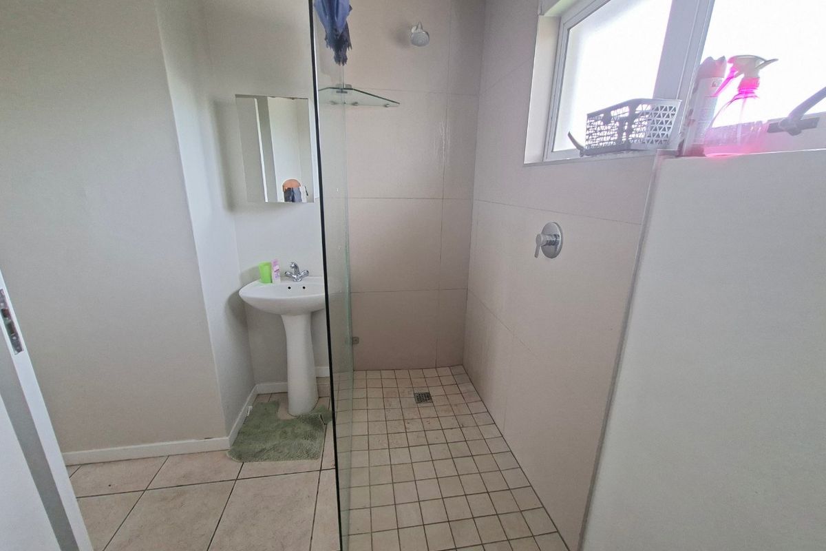 A functional bathroom featuring a pedestal basin, a walk-in shower with a glass screen, and neutral wall and floor tiling.