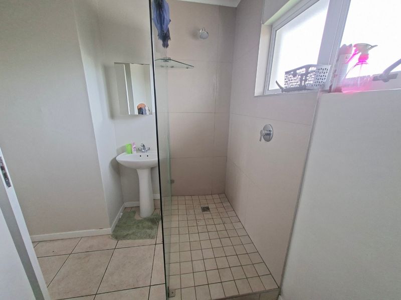 A functional bathroom featuring a pedestal basin, a walk-in shower with a glass screen, and neutral wall and floor tiling.