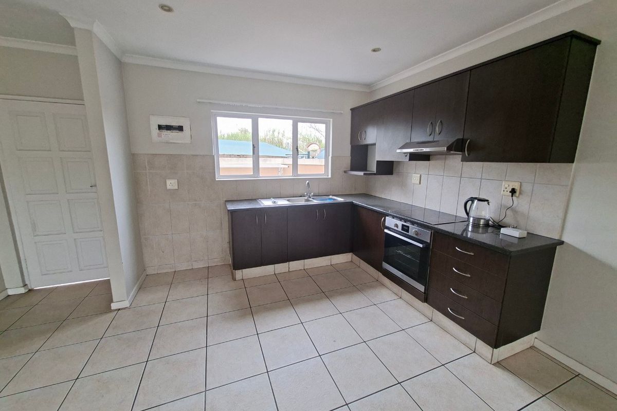A functional kitchen featuring dark wood cabinetry, granite countertops, built-in oven, extractor fan, and tiled flooring with a neutral backsplash.