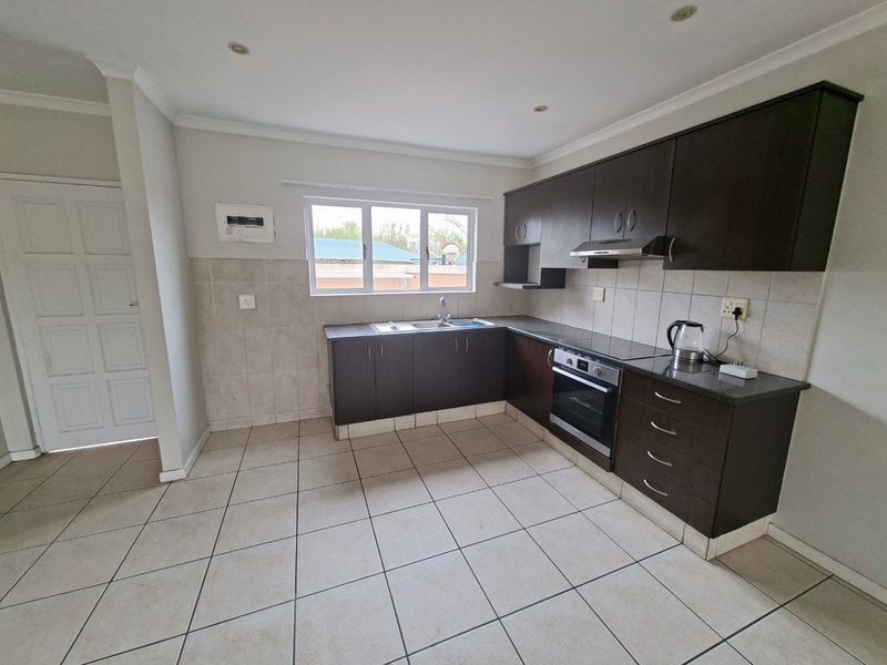 A functional kitchen featuring dark wood cabinetry, granite countertops, built-in oven, extractor fan, and tiled flooring with a neutral backsplash.
