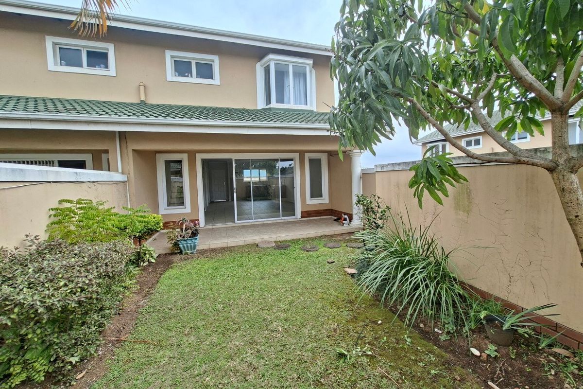 Rear view of the townhouse featuring a private garden, tiled patio area, and sliding glass doors leading into the main living space.