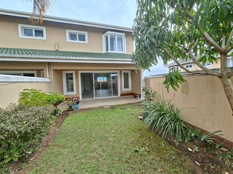 Rear view of the townhouse featuring a private garden, tiled patio area, and sliding glass doors leading into the main living space.