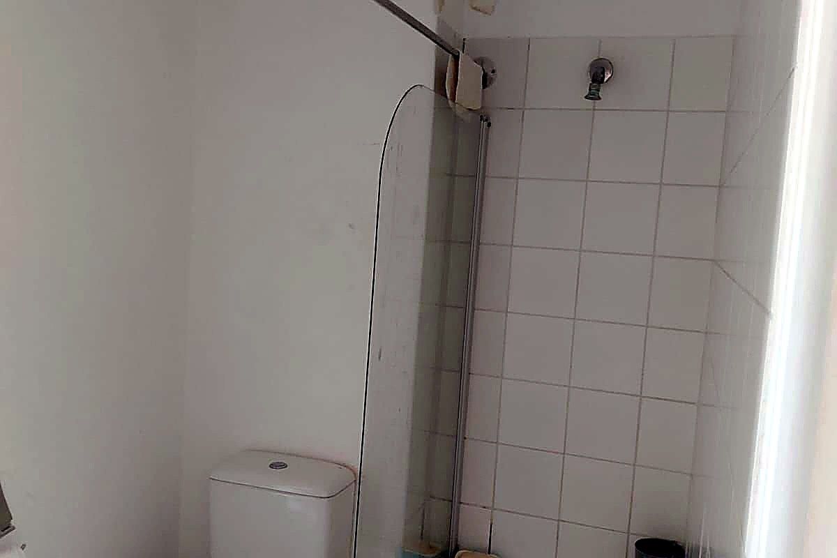A compact bathroom featuring a bathtub with a shower head, glass screen, and toilet. The space requires cosmetic updates to improve its overall condition.