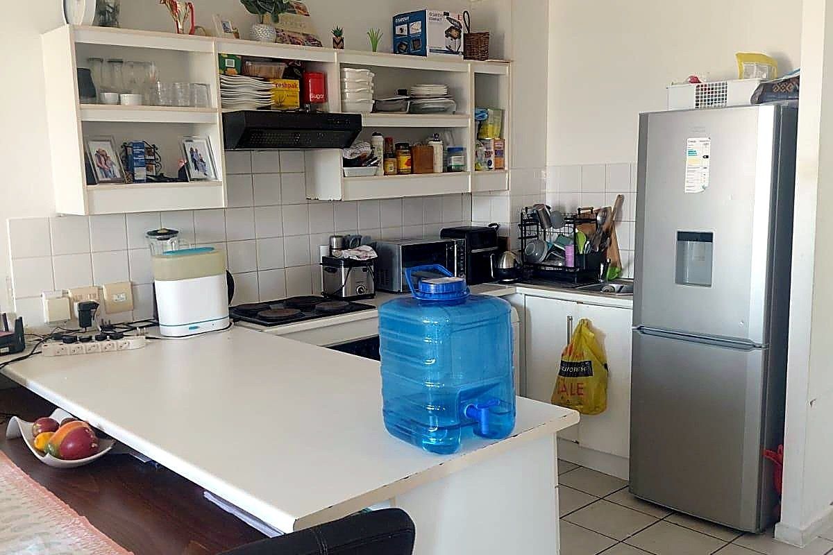 Functional kitchen featuring white cabinetry, tiled splashback, built-in hob with extractor fan, and a breakfast counter, with tiled flooring throughout.