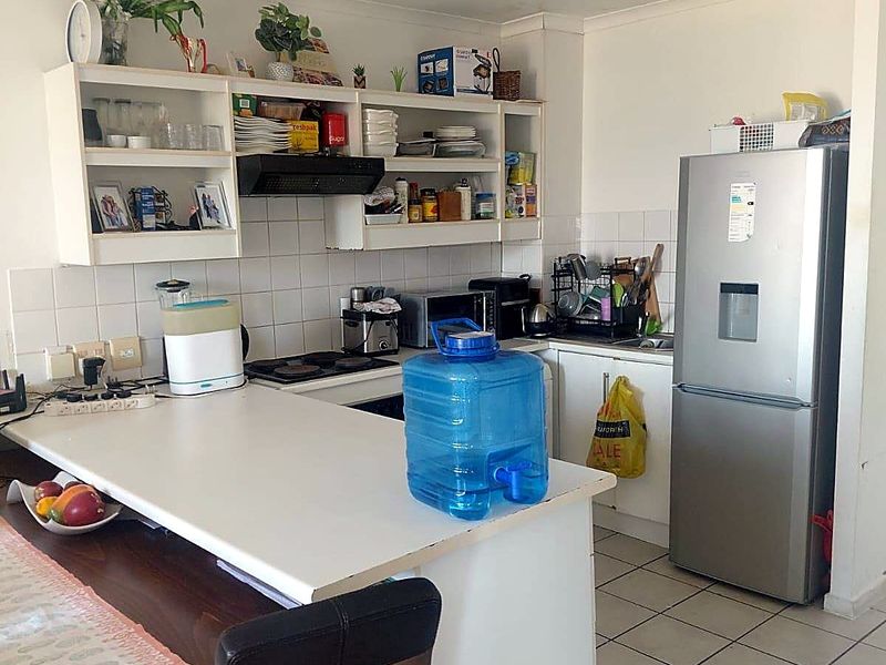 Functional kitchen featuring white cabinetry, tiled splashback, built-in hob with extractor fan, and a breakfast counter, with tiled flooring throughout.