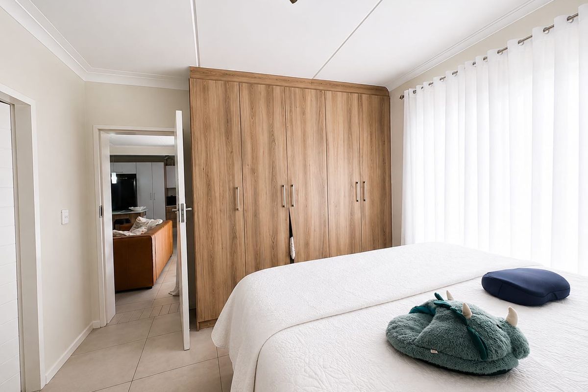 A well-maintained bedroom featuring light-toned tiled flooring, neutral walls, and extensive built-in wooden cabinetry for storage.