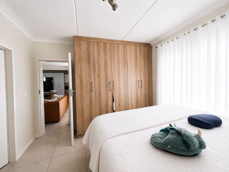 A well-maintained bedroom featuring light-toned tiled flooring, neutral walls, and extensive built-in wooden cabinetry for storage.