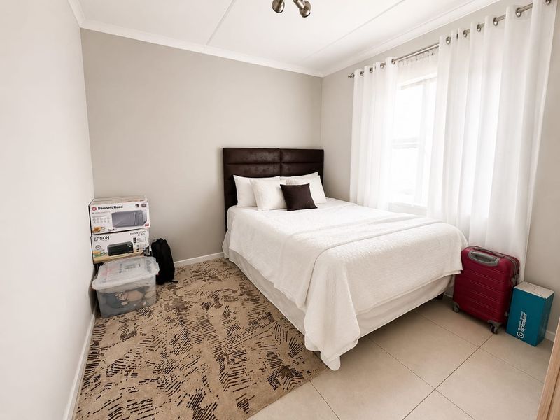A well-maintained bedroom featuring neutral wall tones, tiled flooring, and a window fitted with a curtain rod.