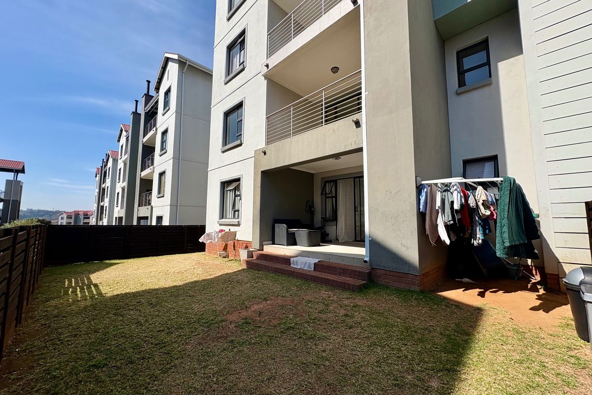 Rear view of the apartment building featuring a private garden, paved patio area with brick steps, and upper-level balconies with metal railings.