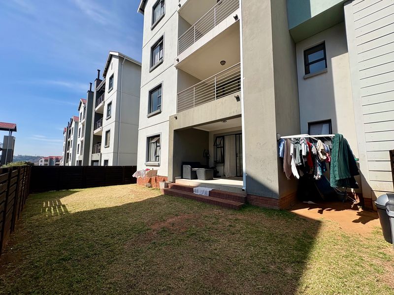 Rear view of the apartment building featuring a private garden, paved patio area with brick steps, and upper-level balconies with metal railings.