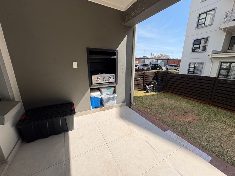 Covered patio area featuring a built-in braai, tiled flooring, and direct access to a private garden space.