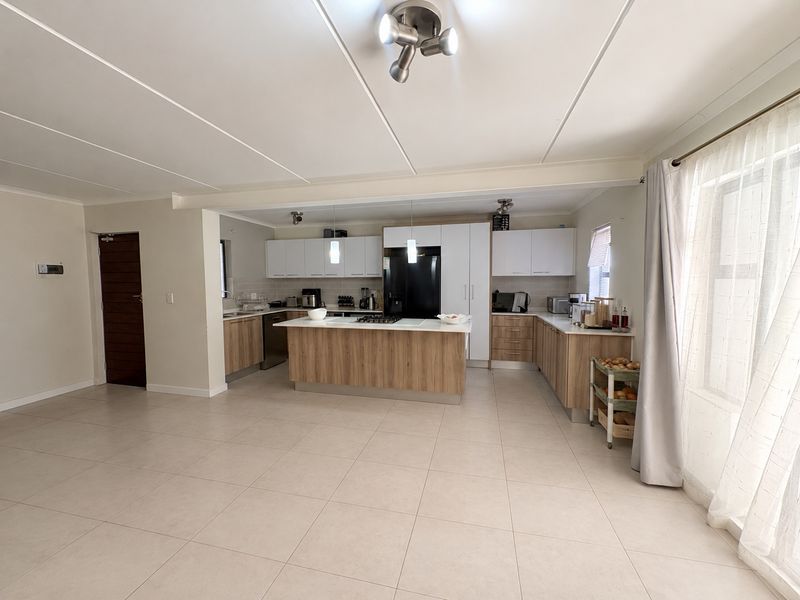 Modern open-plan kitchen featuring a central island, light wood-finish cabinetry, white countertops, and tiled flooring, seamlessly integrated into the living space.