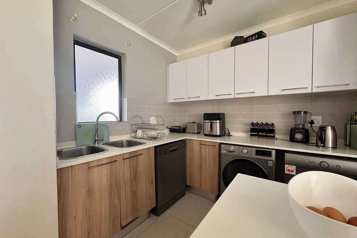 A functional kitchen featuring wood-look lower cabinetry, white upper cabinets, stone countertops, a double sink, and integrated laundry and dishwasher appliances.