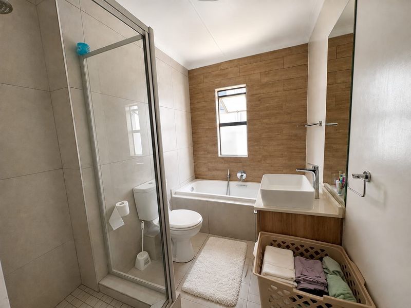 Modern bathroom featuring a glass-enclosed shower, a built-in bathtub, a vessel sink vanity, and contemporary wood-look tile accents.