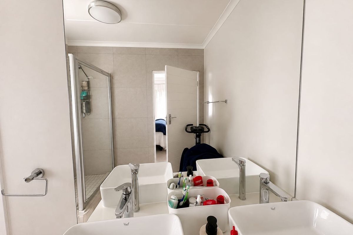 Modern bathroom featuring a double vanity with vessel sinks, a large wall mirror, and a glass-enclosed shower with neutral tiling.