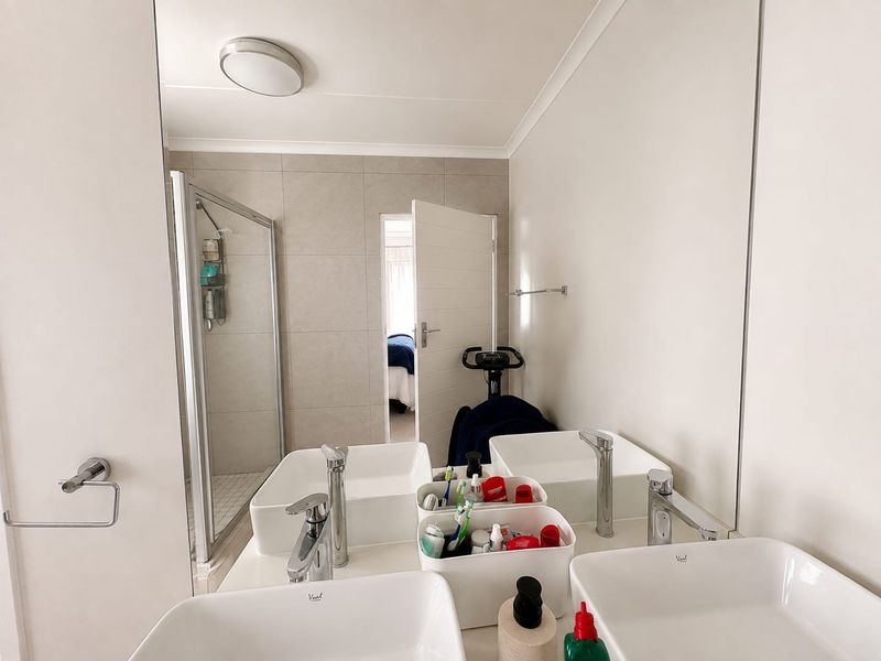 Modern bathroom featuring a double vanity with vessel sinks, a large wall mirror, and a glass-enclosed shower with neutral tiling.