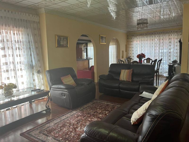 Spacious living room featuring arched doorways, hardwood flooring, and a decorative tiled ceiling with a central crystal chandelier.