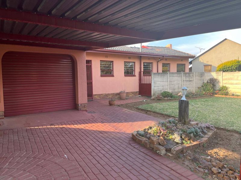 Front exterior view featuring a covered carport, paved driveway, and a small garden area with a precast concrete boundary wall.