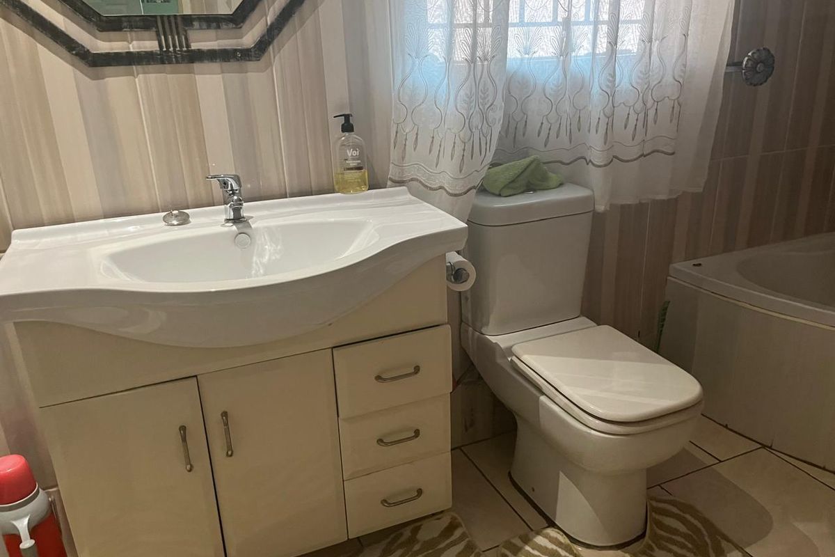 A functional bathroom featuring a vanity cabinet with integrated basin, a standard toilet, and a bathtub with tiled wall finishes.