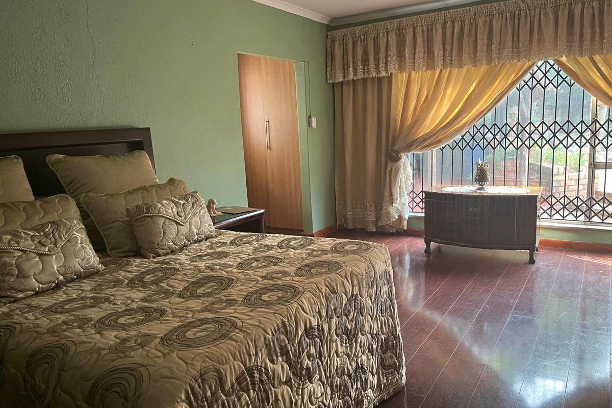 A spacious bedroom featuring laminate flooring, built-in cupboards, and a large window with security bars, offering a functional and comfortable living space.