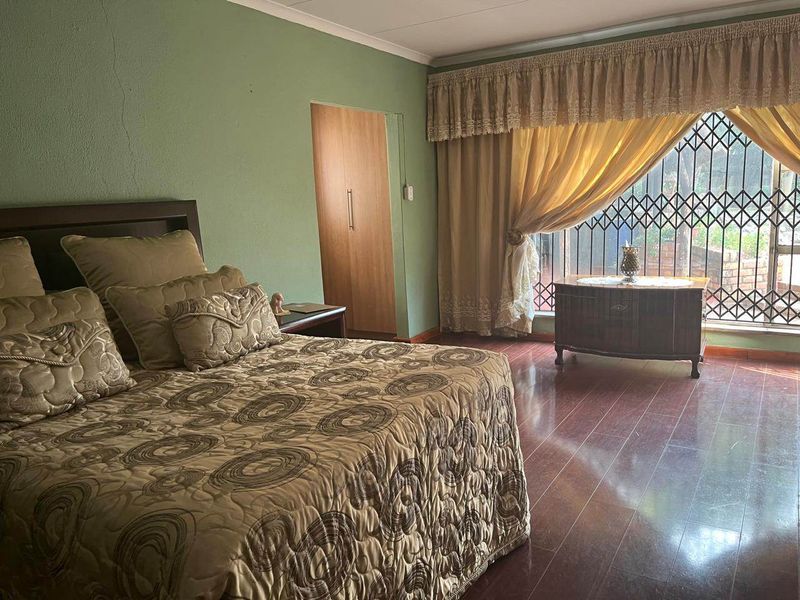 A spacious bedroom featuring laminate flooring, built-in cupboards, and a large window with security bars, offering a functional and comfortable living space.
