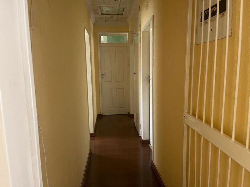 A narrow residential hallway featuring laminate flooring, a security gate, and a drop ceiling, requiring cosmetic updates to improve the overall aesthetic.
