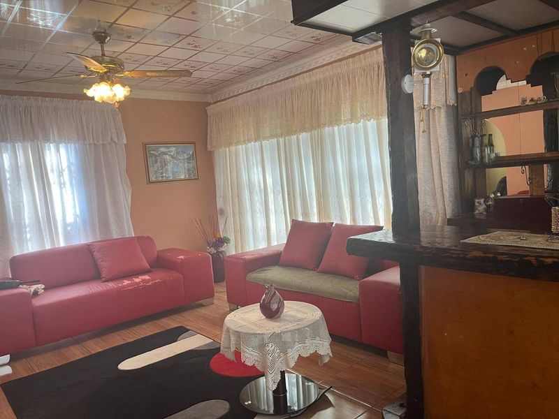 Living room featuring tiled flooring, a ceiling fan, and a built-in bar counter, offering a dated interior space with potential for modernization.