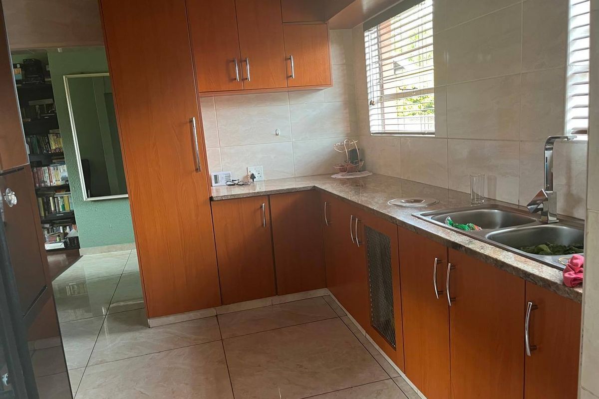 A functional kitchen featuring wood-look cabinetry, laminate countertops, a double stainless steel sink, and tiled flooring with natural light from the window.