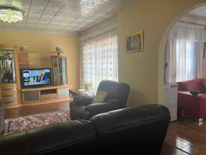 A living room featuring laminate flooring, a decorative tiled ceiling, and an arched entryway leading to an adjacent space.