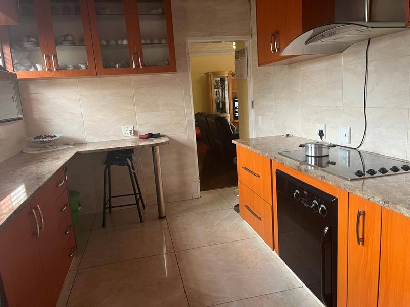 A functional kitchen featuring wood-finish cabinetry, laminate countertops, a built-in oven, and an electric hob with an extractor fan.