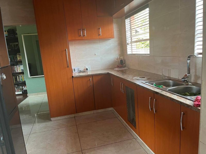 A functional kitchen featuring wood-look cabinetry, laminate countertops, a double stainless steel sink, and tiled flooring with natural light from the window.