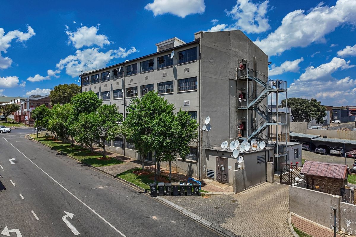 Aerial view of a multi-story apartment building featuring an external metal staircase, paved driveway, and multiple satellite dish installations.