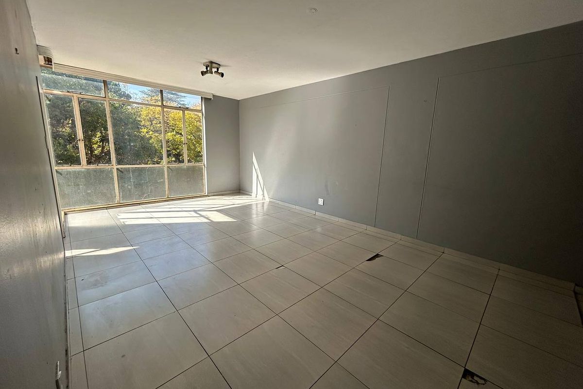 An empty living room featuring large windows and tiled flooring, requiring some maintenance to the floor tiles.