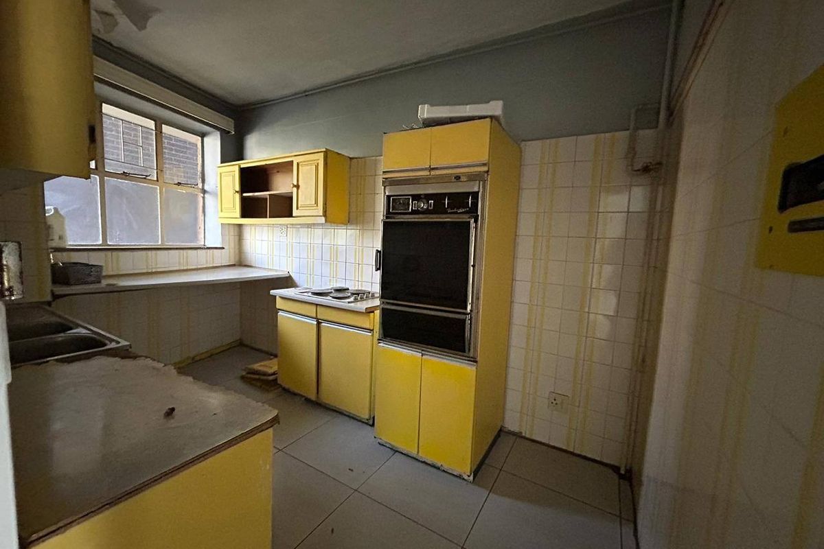 A dated kitchen featuring original yellow cabinetry, built-in oven, cooktop, and tiled finishes, offering significant potential for a modern renovation.
