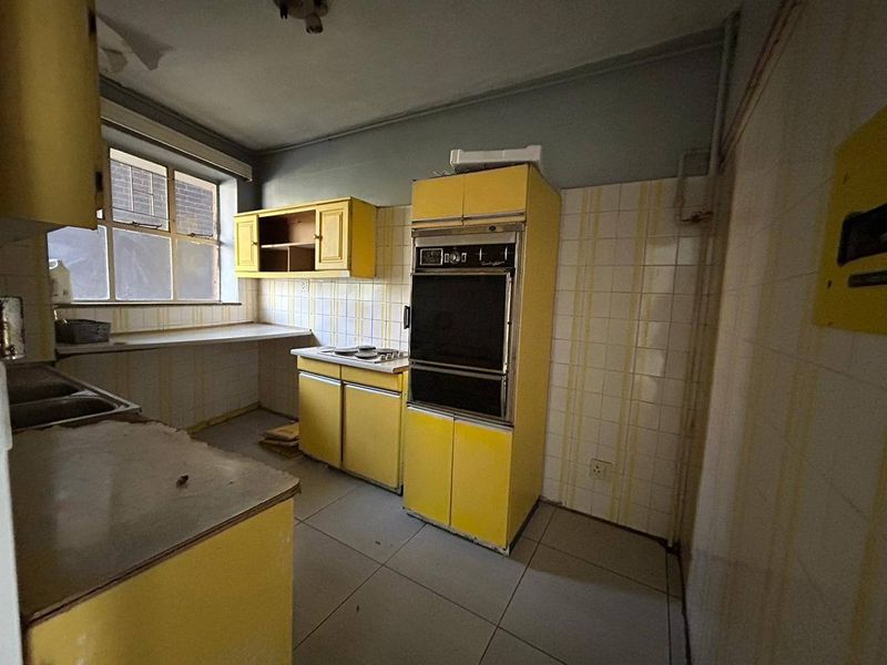 A dated kitchen featuring original yellow cabinetry, built-in oven, cooktop, and tiled finishes, offering significant potential for a modern renovation.