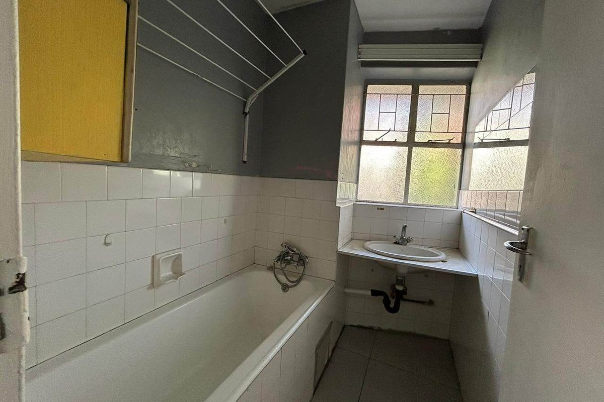 A dated bathroom featuring a bathtub, wall-mounted basin, and tiled splashbacks, requiring renovation to modernize the space and improve overall condition.