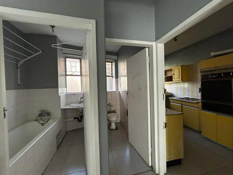 A hallway view showing access to a bathroom, separate toilet, and a dated kitchen with built-in cabinetry and appliances.