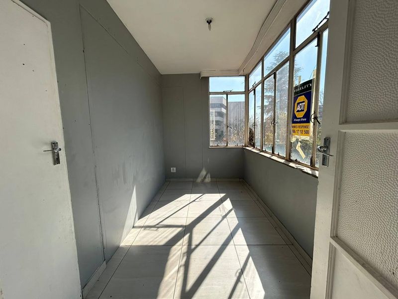 An empty, enclosed balcony or sunroom featuring tiled flooring and large windows, offering a bright space suitable for a home office or reading nook.