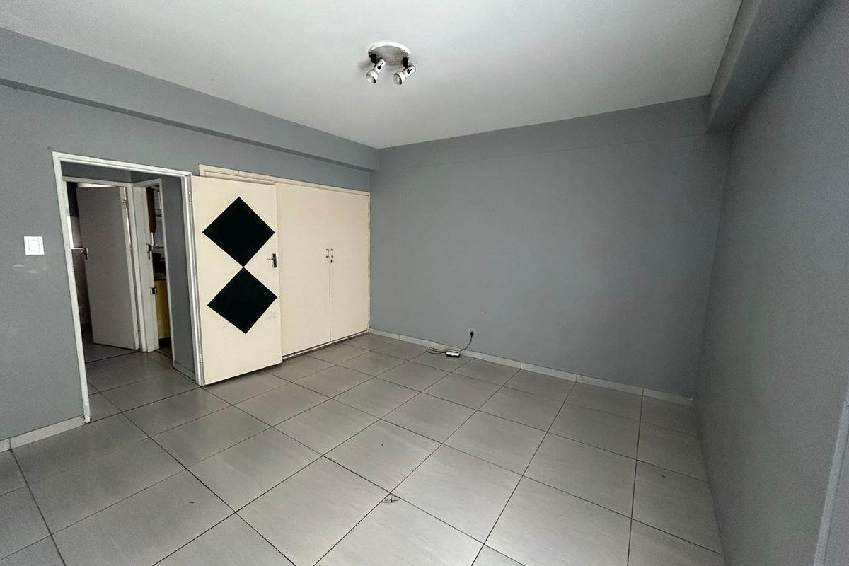 An empty bedroom featuring grey walls, tiled flooring, and built-in cupboards with a simple spotlight fixture.