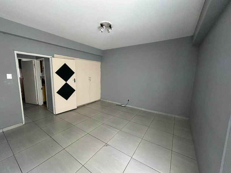 An empty bedroom featuring grey walls, tiled flooring, and built-in cupboards with a simple spotlight fixture.