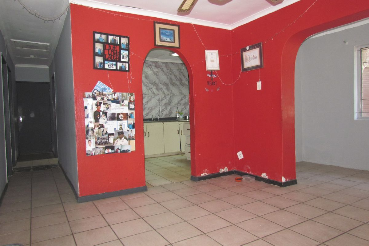 An open-plan living area featuring tiled floors and arched entryways leading to the kitchen, showing signs of wear on the lower wall sections.