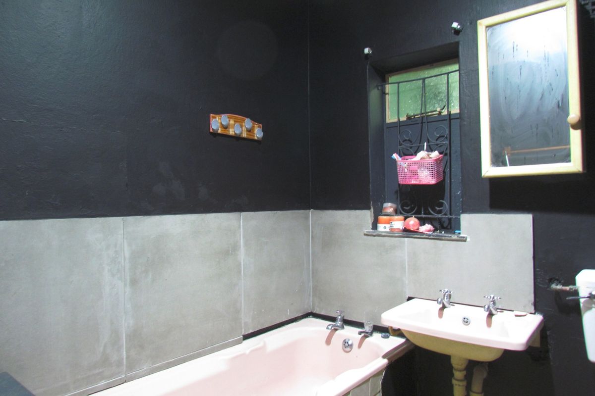 A bathroom featuring a bathtub and wall-mounted basin with dark painted walls and tiled splashbacks, requiring cosmetic updates to improve the overall aesthetic.