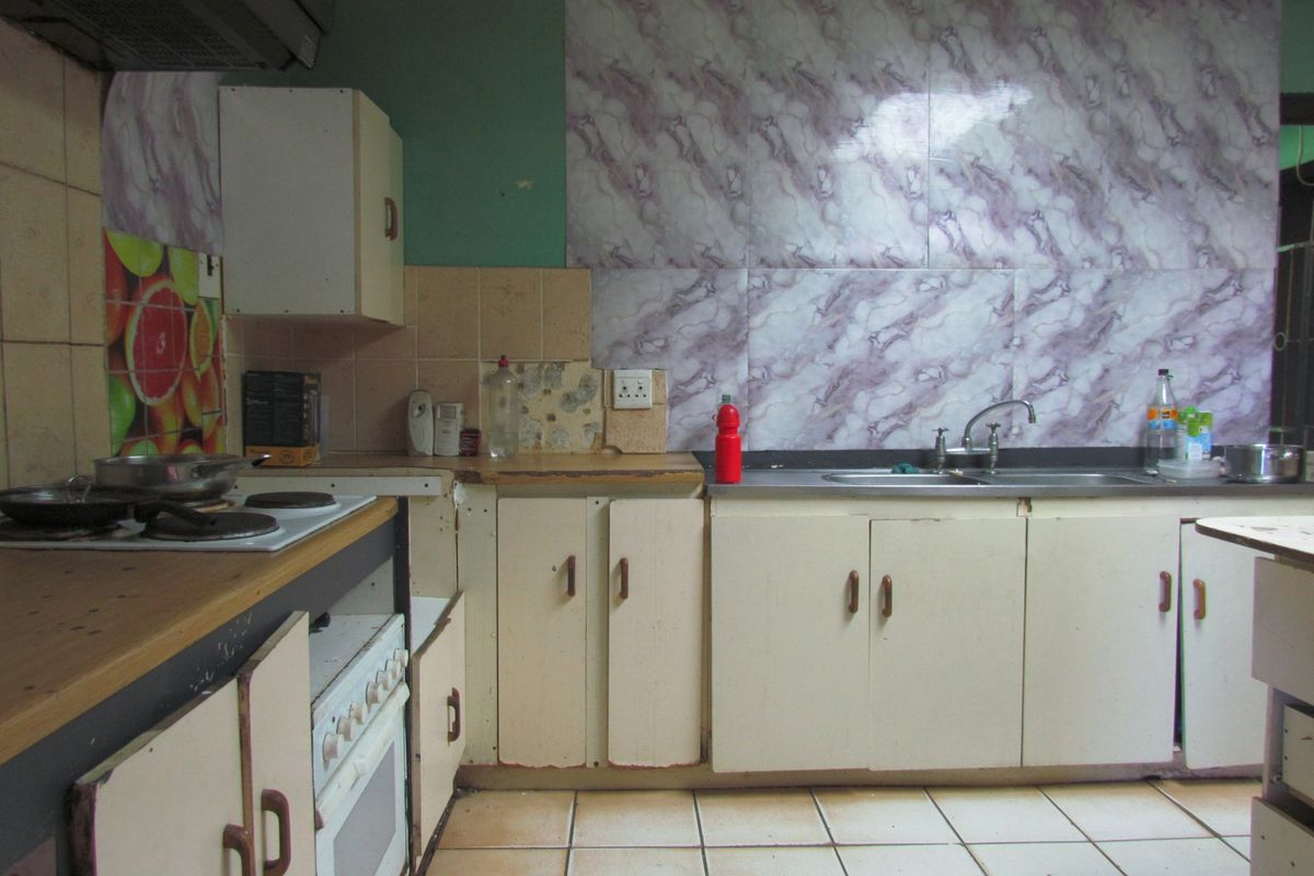 A dated kitchen featuring original cabinetry, a built-in stove with extractor fan, and tiled splashbacks, offering significant potential for modernization and renovation.